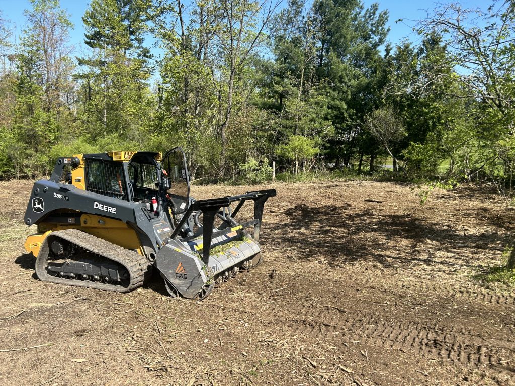 Tracked skid steer with a forestry mulcher head clearing a lot