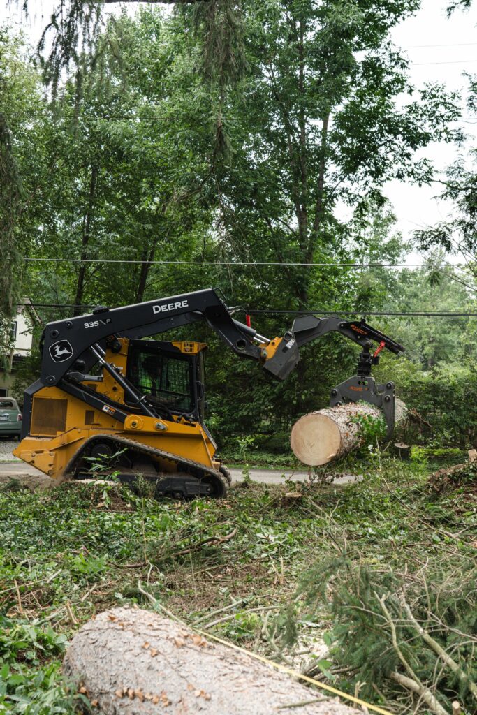 Tracked loader carrying a large cut log section away from a residential driveway